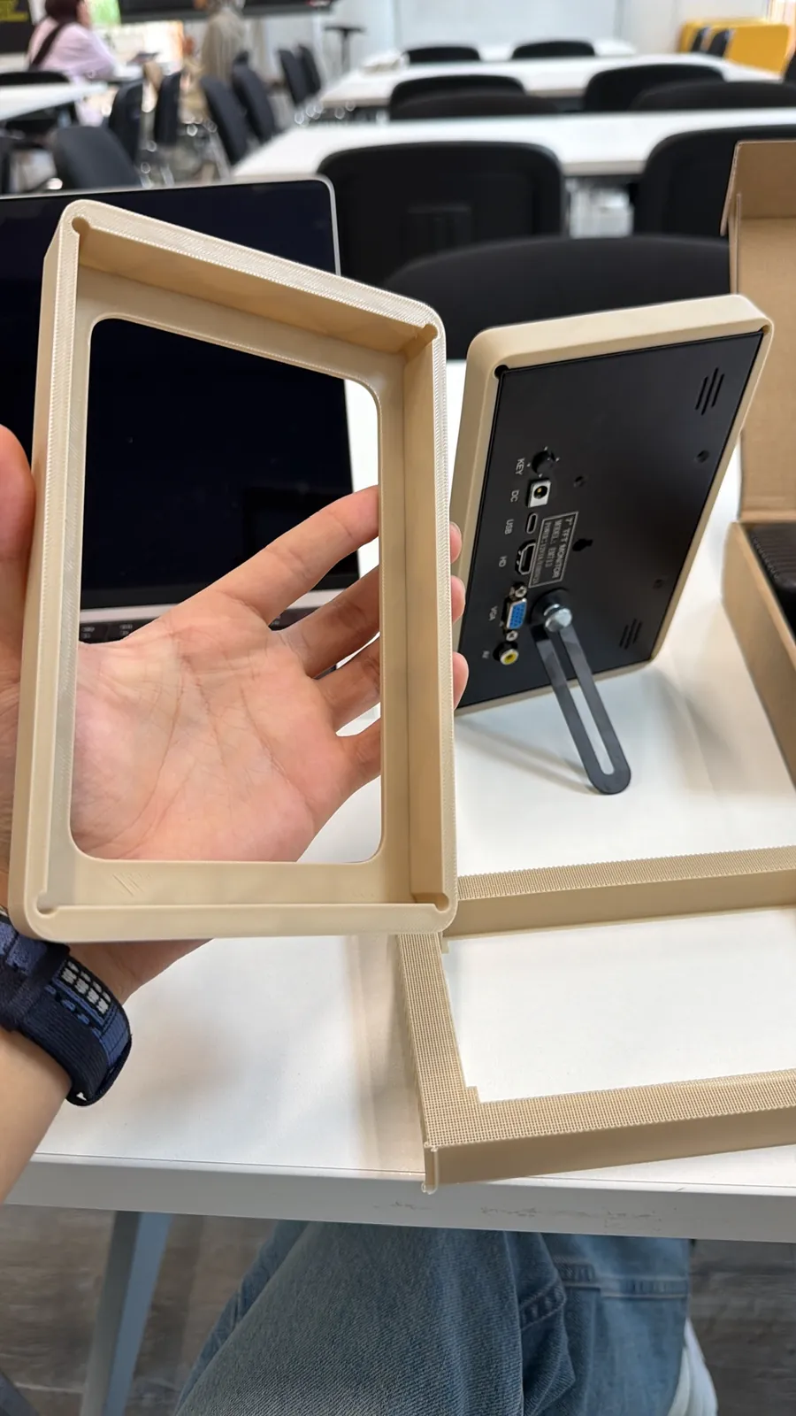 Hand holding printed screen cover test pieces next to the monitor
