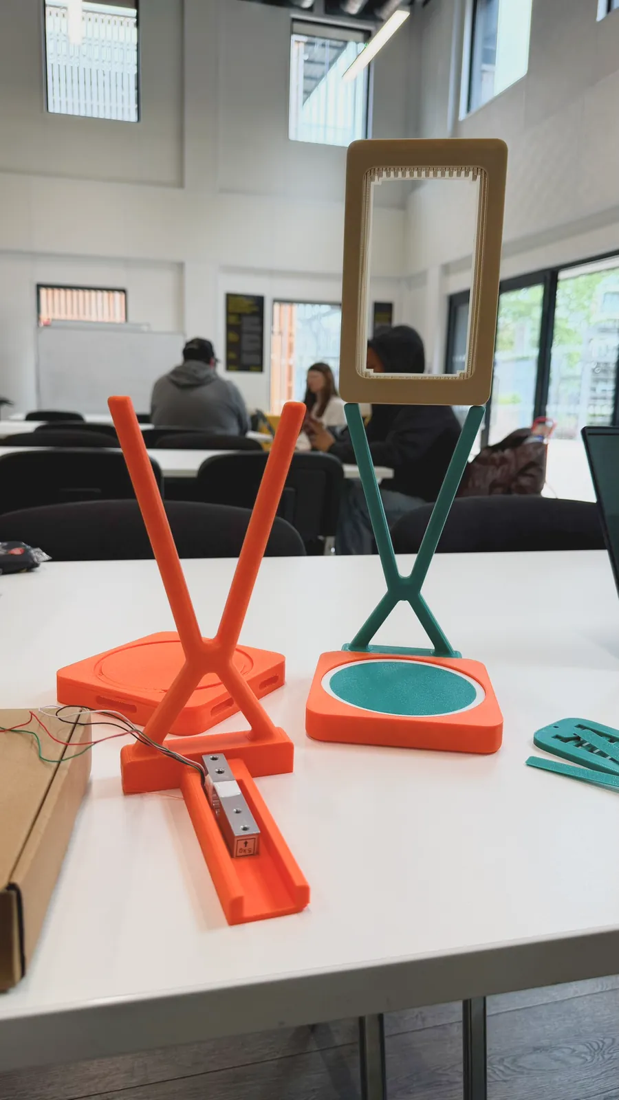 Printed stand iterations in orange and green on a table, with a cardboard screen frame