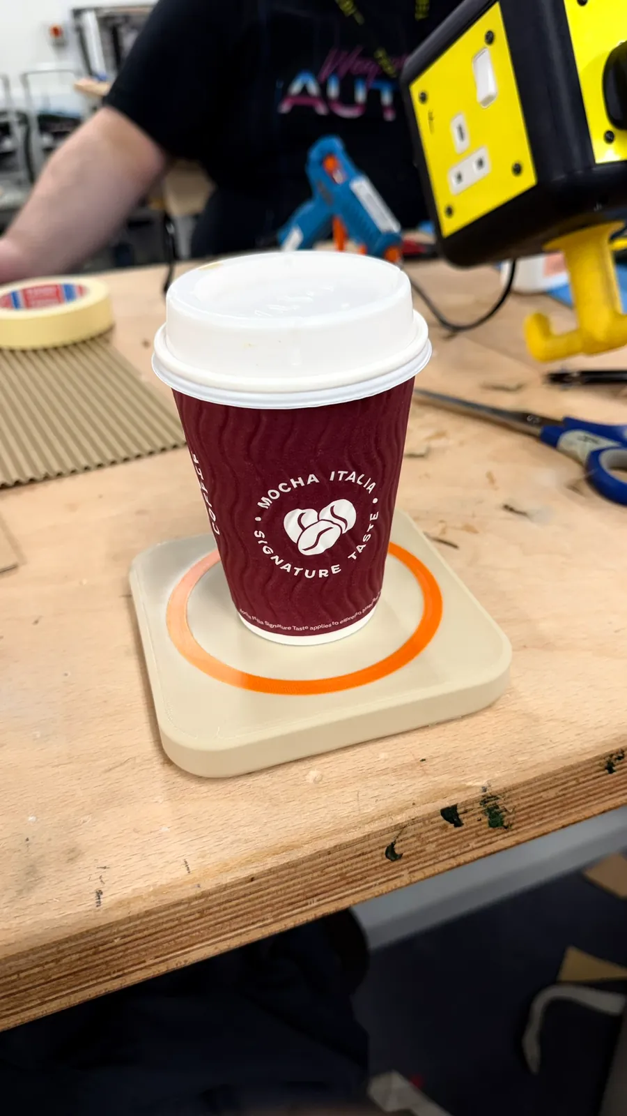 A takeaway cup on a printed coaster with an orange ring