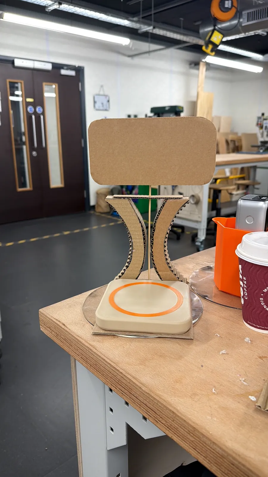 Cardboard hourglass-shaped stand holding a cardboard screen above a coaster