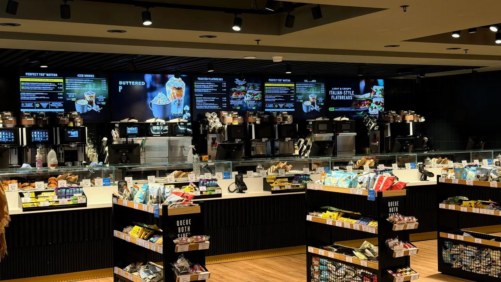 A large café with a long service counter and digital menu screens